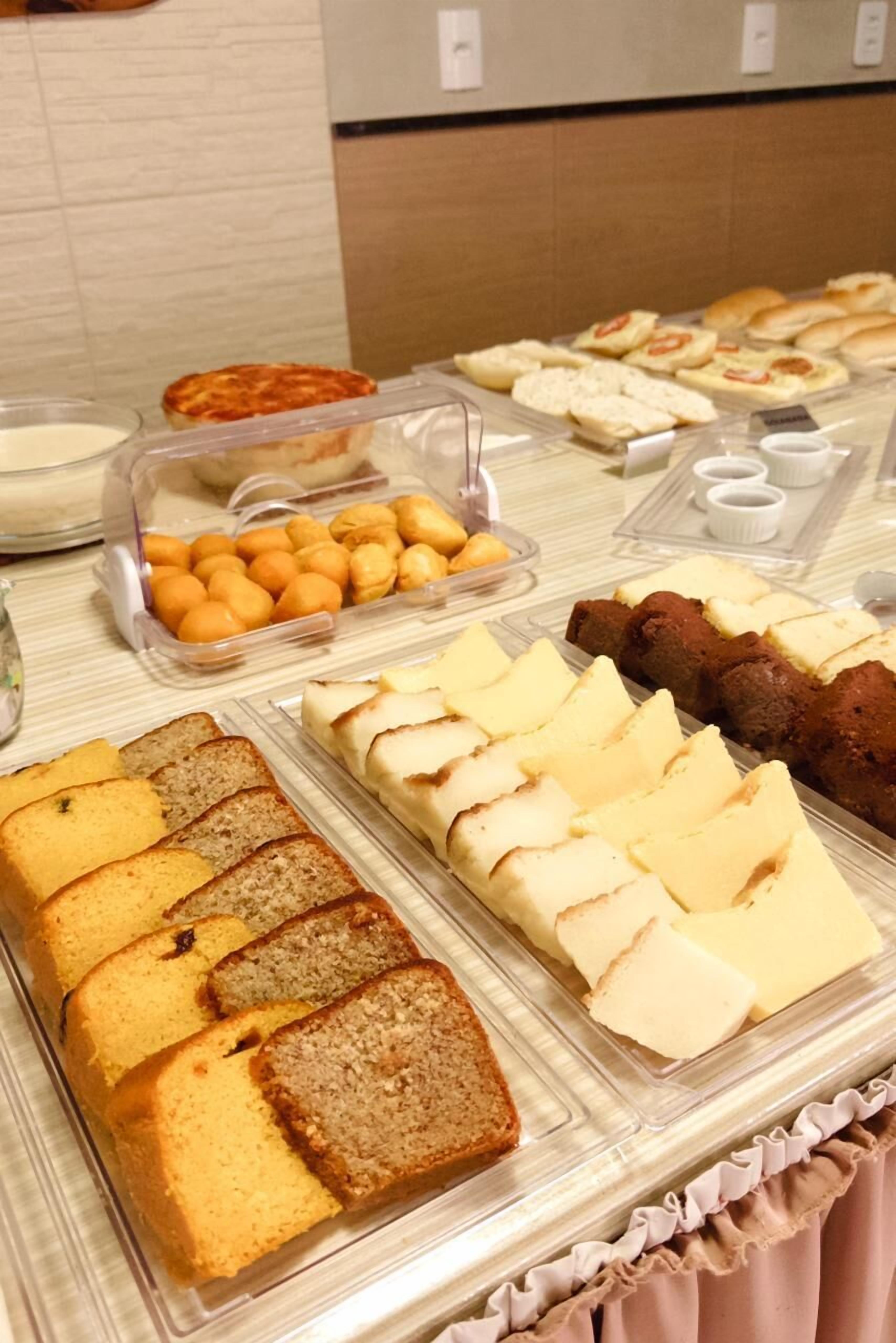 Un bufé con diversas opciones de comida, incluyendo pan, pasteles y un recipiente con frutas cítricas.