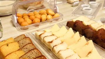 Un bufé con diversas opciones de comida, incluyendo pan, pasteles y un recipiente con frutas cítricas.
