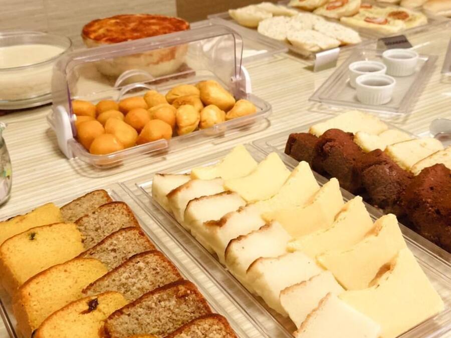 Un bufé con diversas opciones de comida, incluyendo pan, pasteles y un recipiente con frutas cítricas.