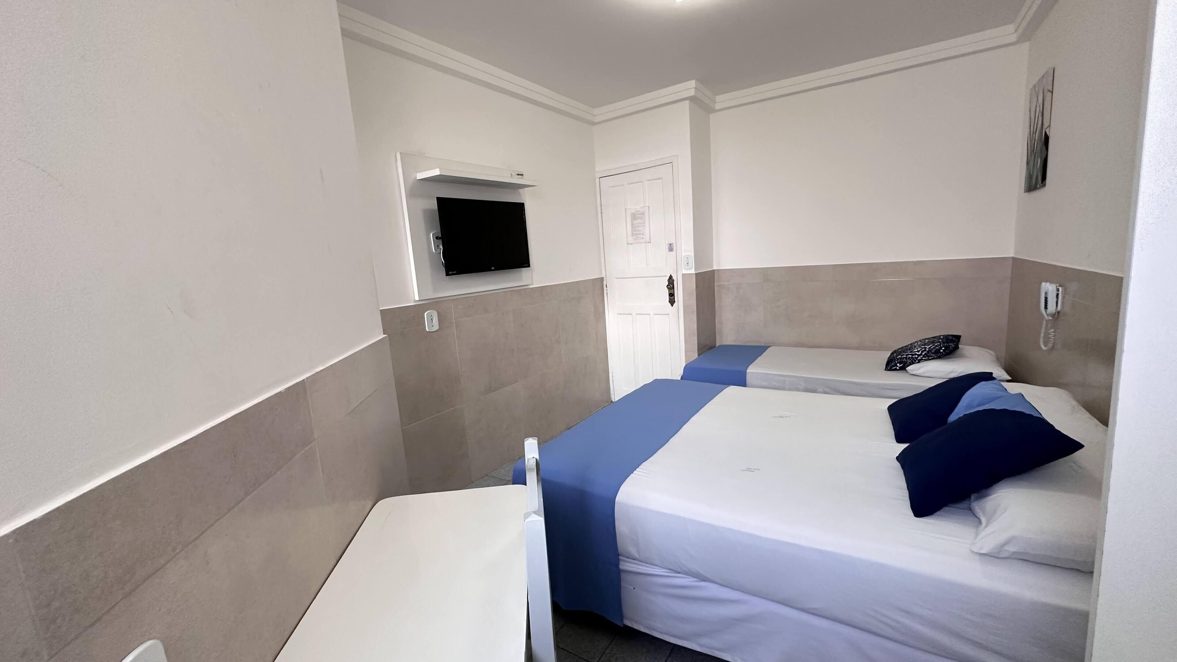 Habitación de hotel con dos camas, una mesita, un televisor fijado a la pared y un teléfono.
