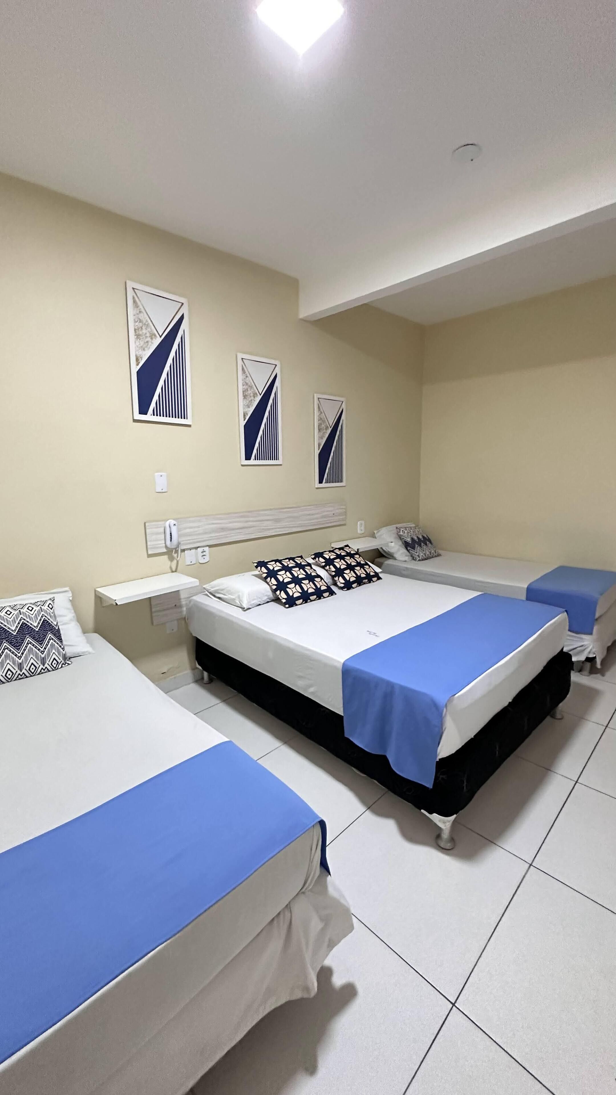 A hotel room with three beds, a bedside table, and a wall-mounted air purifier.