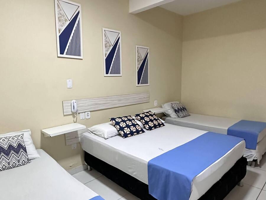 Habitación de hotel con tres camas, una mesita de noche y un purificador de aire de pared.