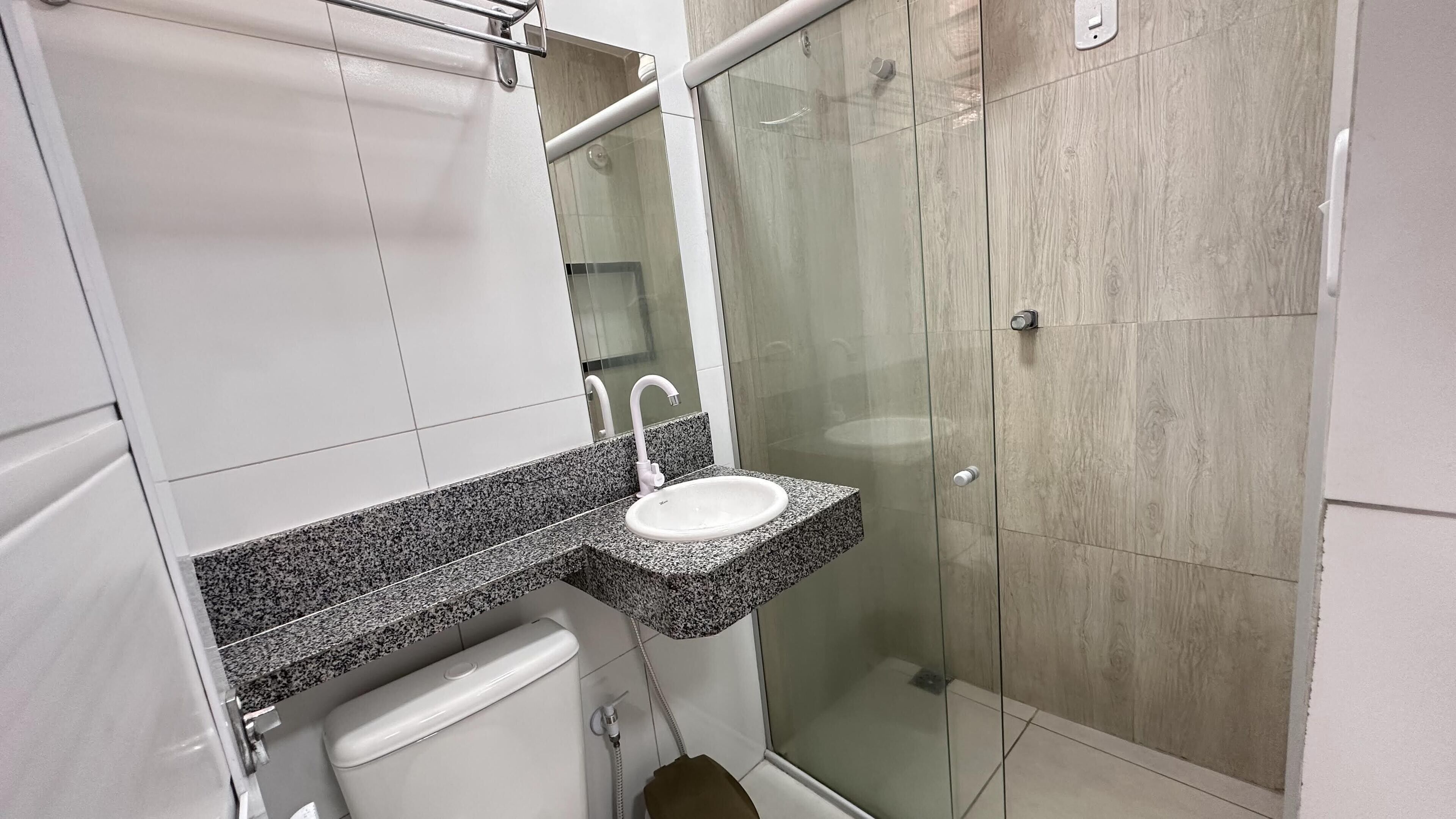 A bathroom with a granite countertop sink, a mirror, a toilet, and a glass shower enclosure.