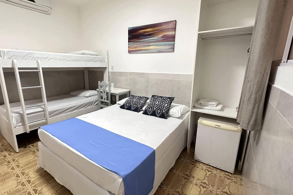 A dormitory room with bunk beds, a desk, a chair, a small refrigerator, and a painting on the wall.
