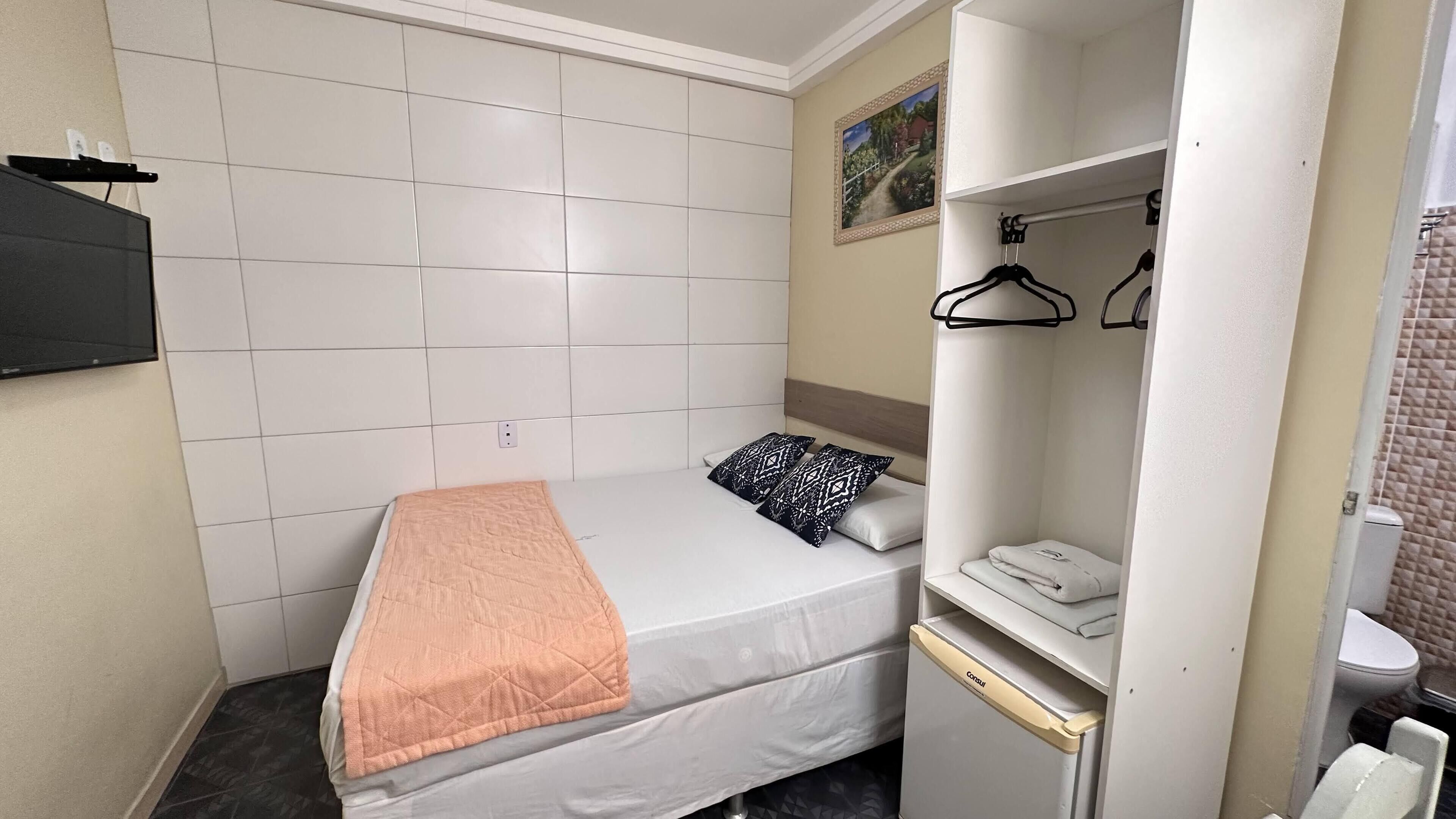 Un dormitorio pequeño y ordenado con una cama, una mesita de noche, un armario y un baño a la vista.