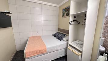 Un dormitorio pequeño y ordenado con una cama, una mesita de noche, un armario y un baño a la vista.