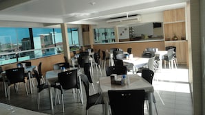 A modern dining area with tables and chairs, large windows, and an air conditioning unit. - Pousada São Luis (Aracaju)