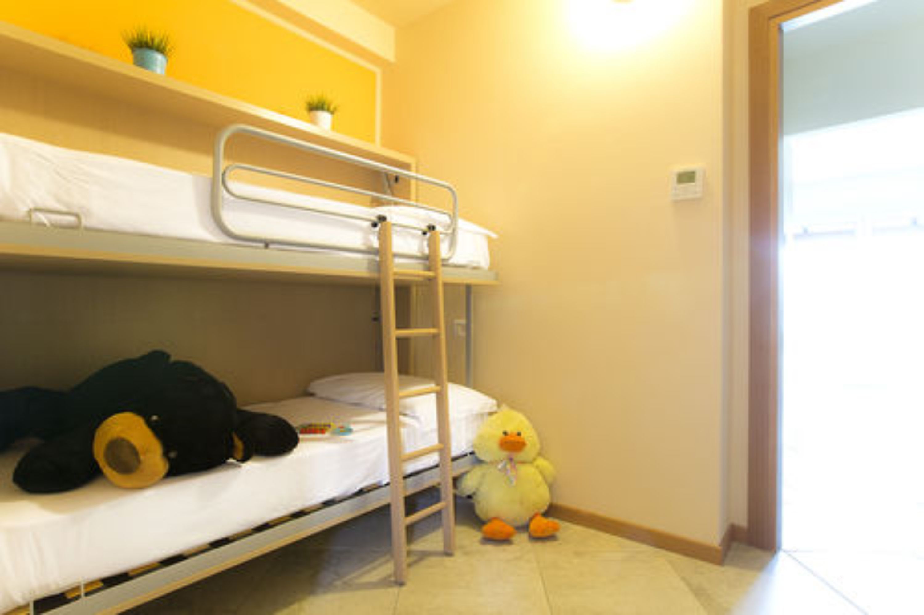 Een stapelbed met een ladder, een pluche teddybeer en een rubberen eend op de vloer.