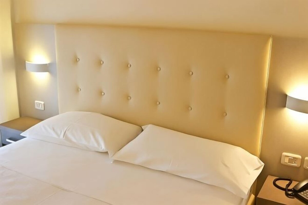A hotel room with a large bed, a headboard with buttons, and two wall-mounted lamps.