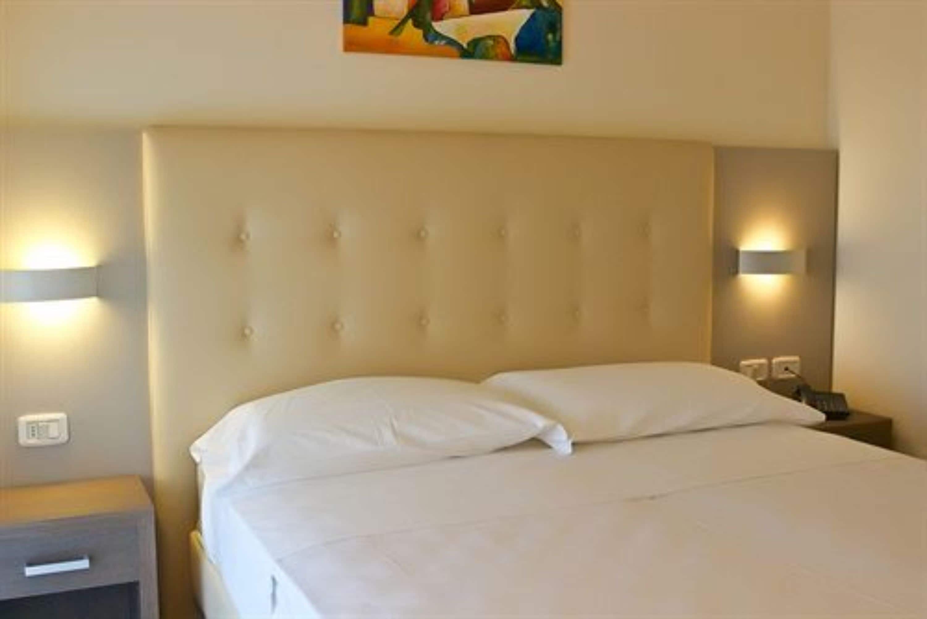 Una habitación de hotel con una cama grande, dos mesitas de noche e iluminación en la pared.