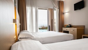 Habitación de hotel con dos camas, un escritorio, un televisor y un balcón con vistas.