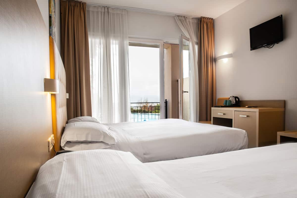 A hotel room with two beds, a desk, a TV, and a balcony with a view.