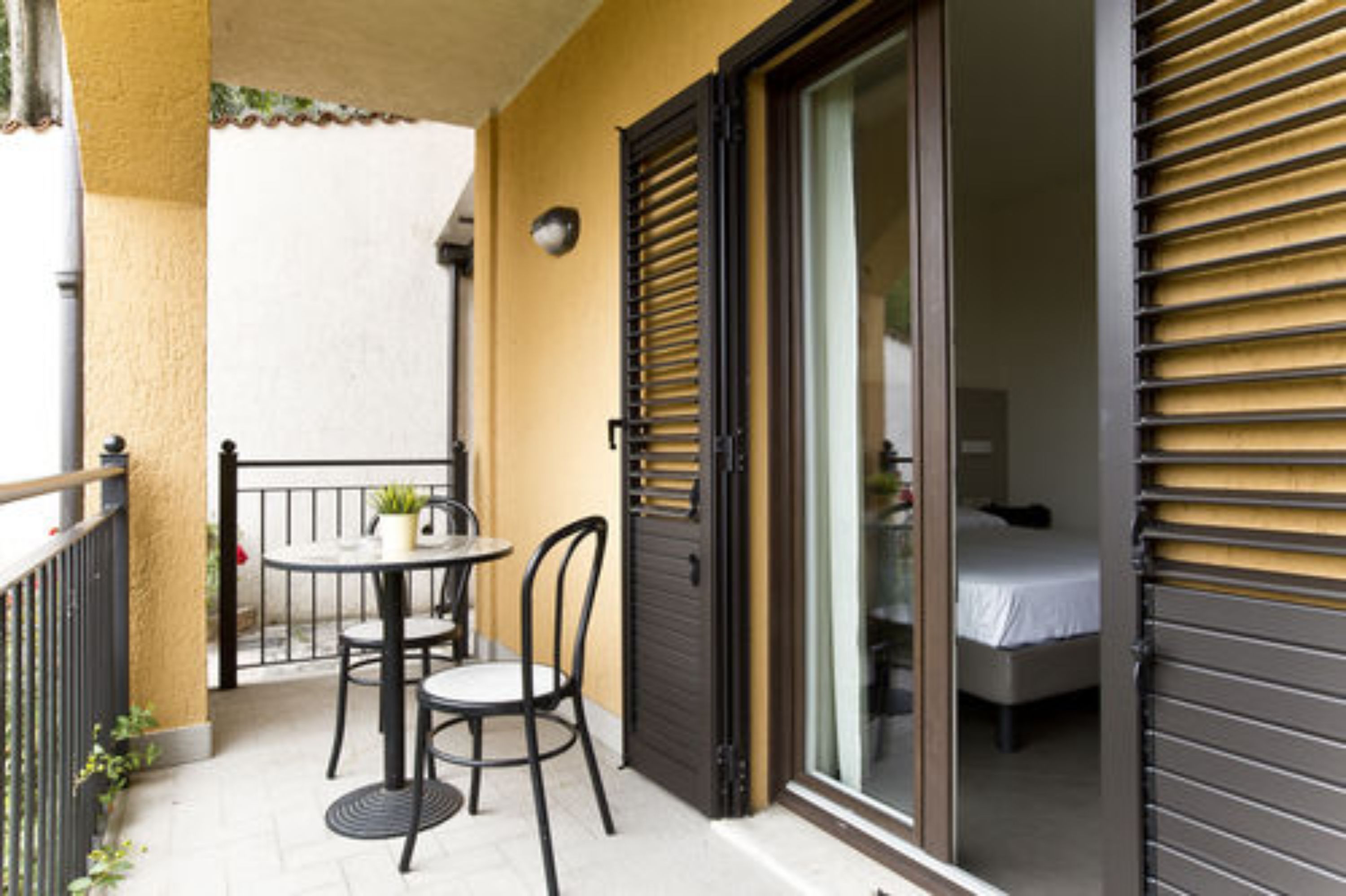 Ein Balkon mit Tisch und Stühlen, eine Schiebetür und ein Bett im Raum sichtbar.