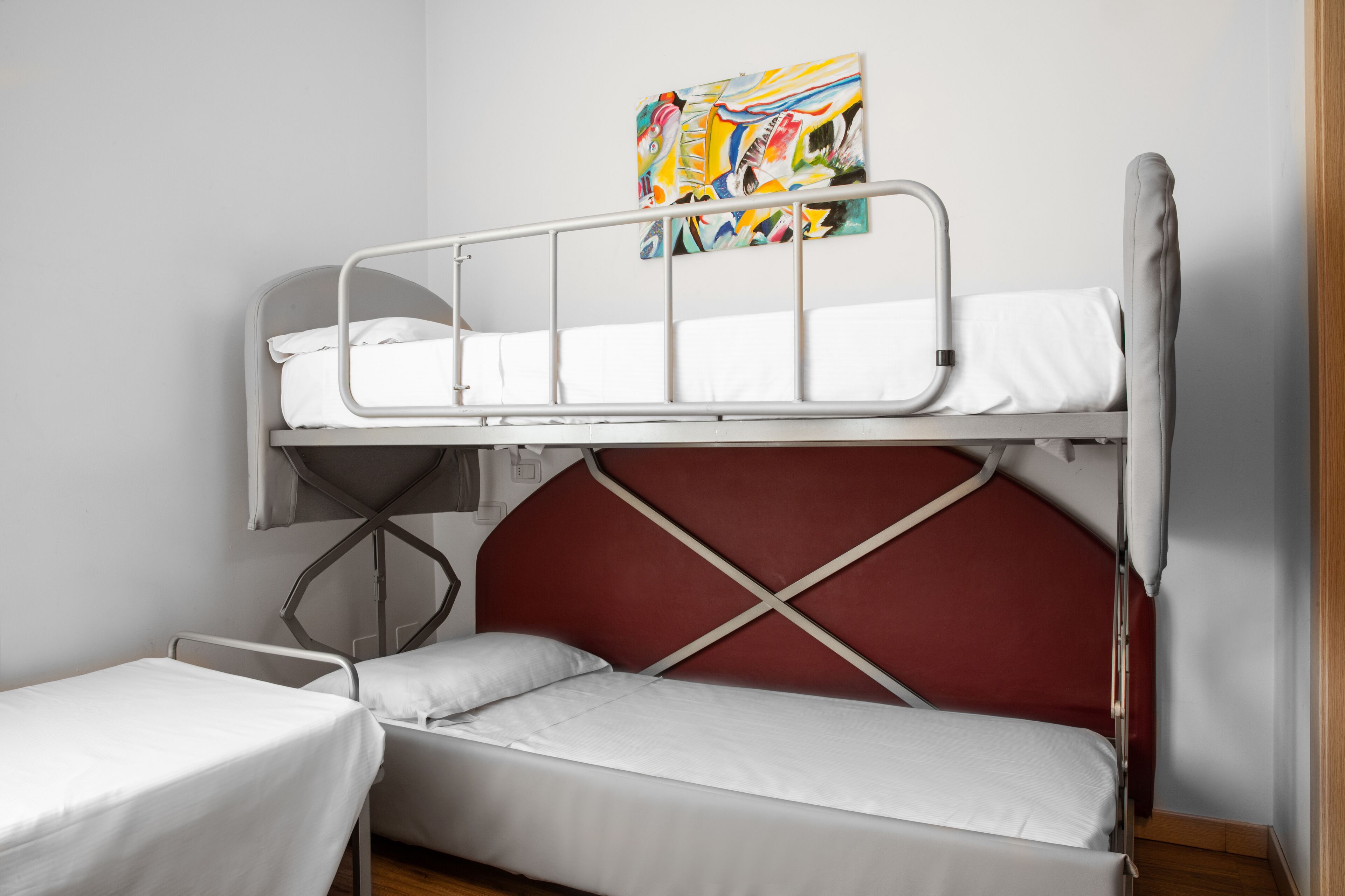 A bunk bed room with a red headboard, a small table, and a colorful painting on the wall.