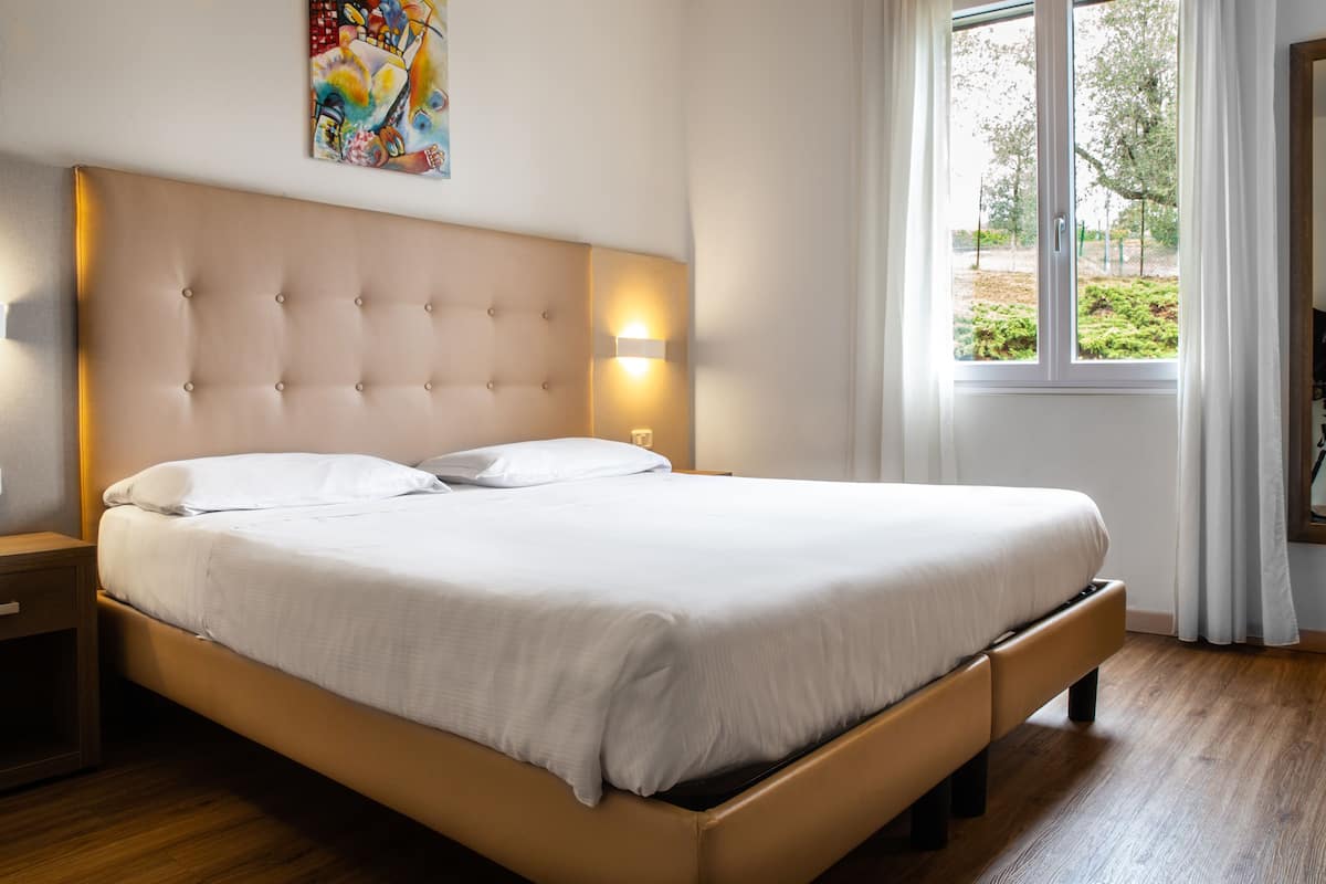 A neatly made bed with a tufted headboard, a bedside table, and a window with curtains.