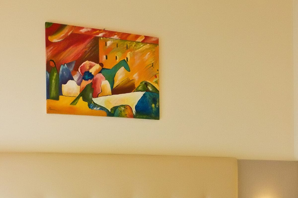 A hotel room with a large bed, a tufted headboard, a painting on the wall, and a bedside lamp.