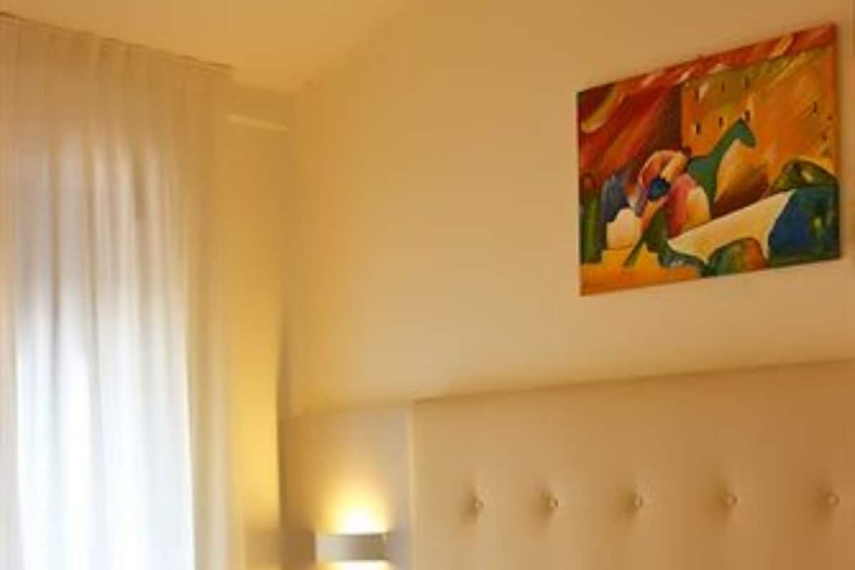 A hotel room with a large bed, a headboard, a painting on the wall, and a window with curtains.