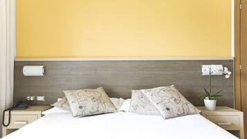 Habitación de hotel con una cama grande, dos almohadas con diseño de mapa, un teléfono en la mesita de noche, una mesita de noche, una lámpara de pared y una orquídea en maceta.