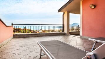 Un balcone con ringhiera in metallo, una poltrona e vista sul mare e montagne in lontananza.