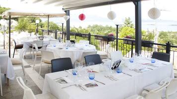 An outdoor dining area with tables set for two, white chairs, and a view of the sea.