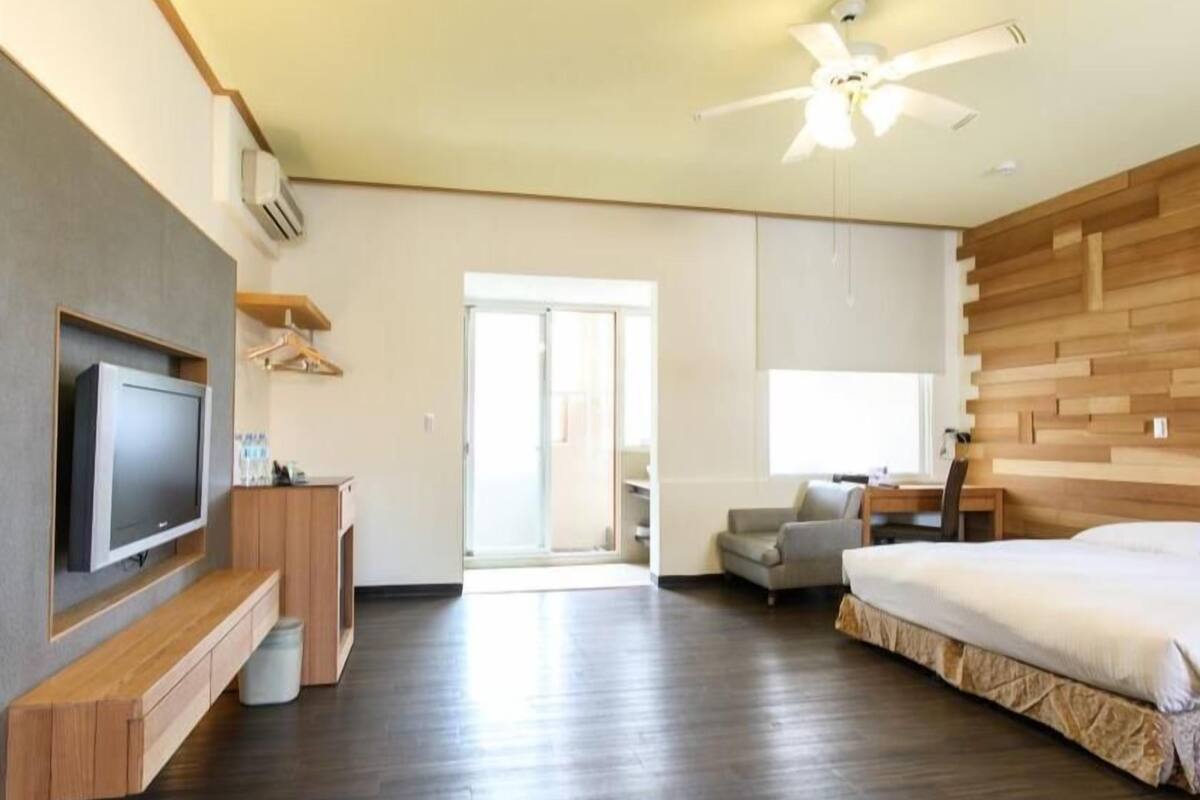 Quarto de hotel moderno com televisão de tela plana, painel de parede em madeira, ventilador de teto e uma cama grande.