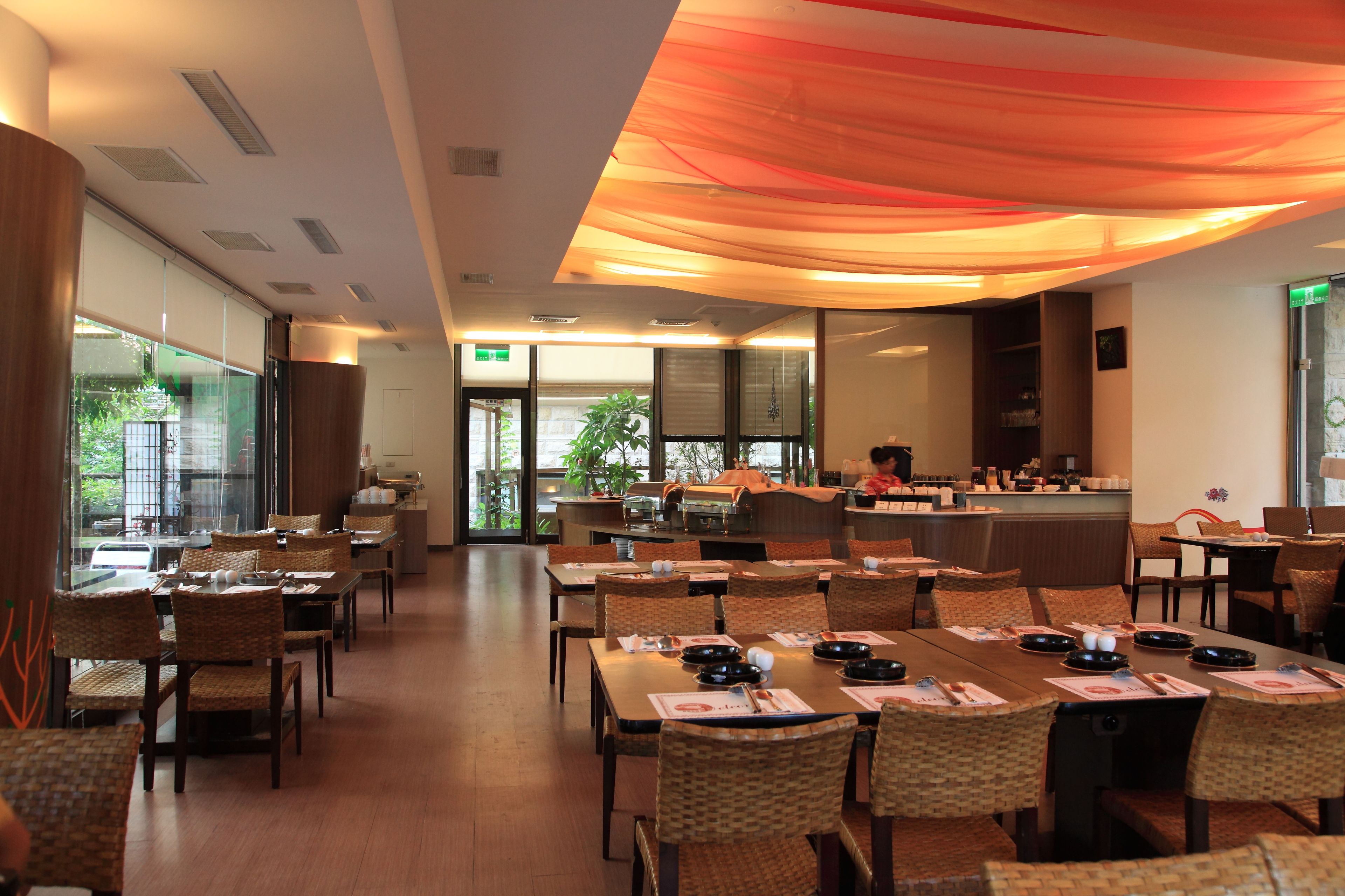 A restaurant with multiple dining tables and chairs, a bar area, and large windows allowing natural light.