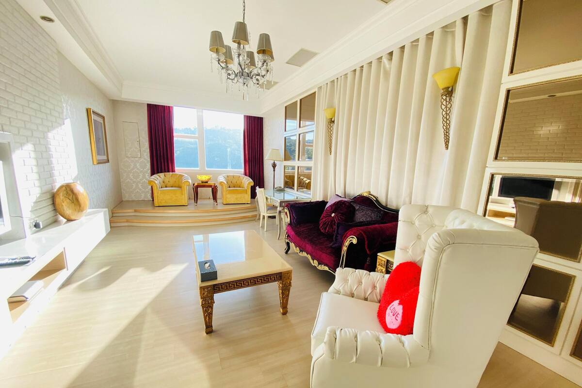 Uma sala de estar espaçosa com um sofá branco, um travesseiro vermelho, uma mesa de centro e um candelabro.