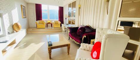 Un salon spacieux avec un canapé blanc, un coussin rouge, une table basse et un lustre.