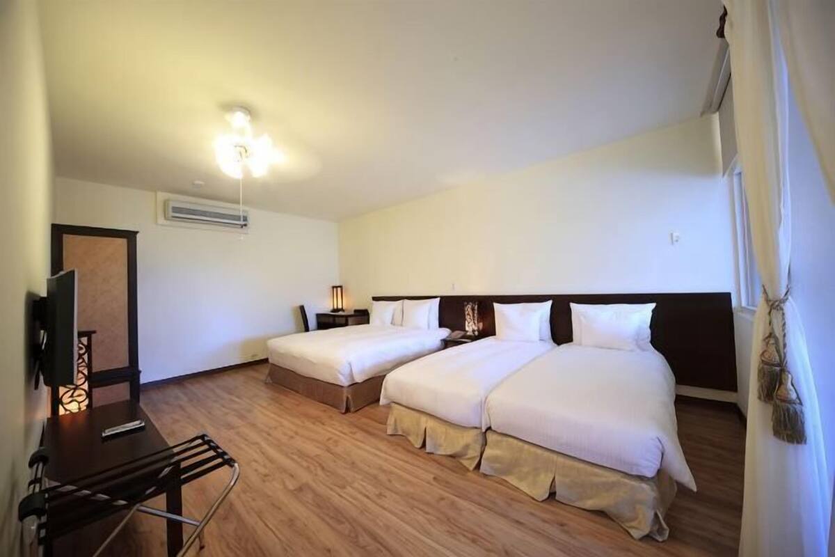 Quarto de hotel com duas camas, televisão, escrivaninha e luminária.