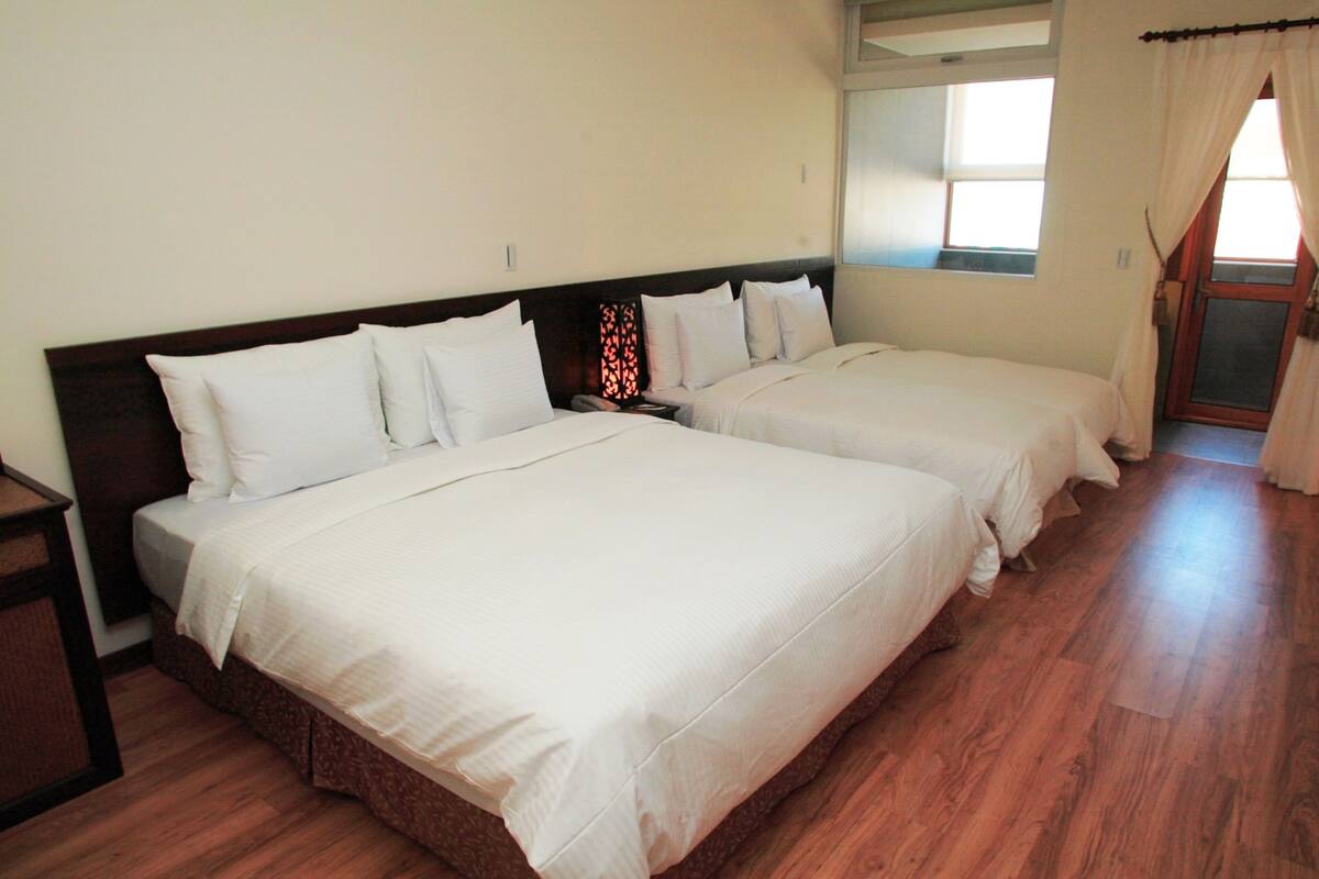 Quarto de hotel com duas camas, piso de madeira e janela com cortinas.