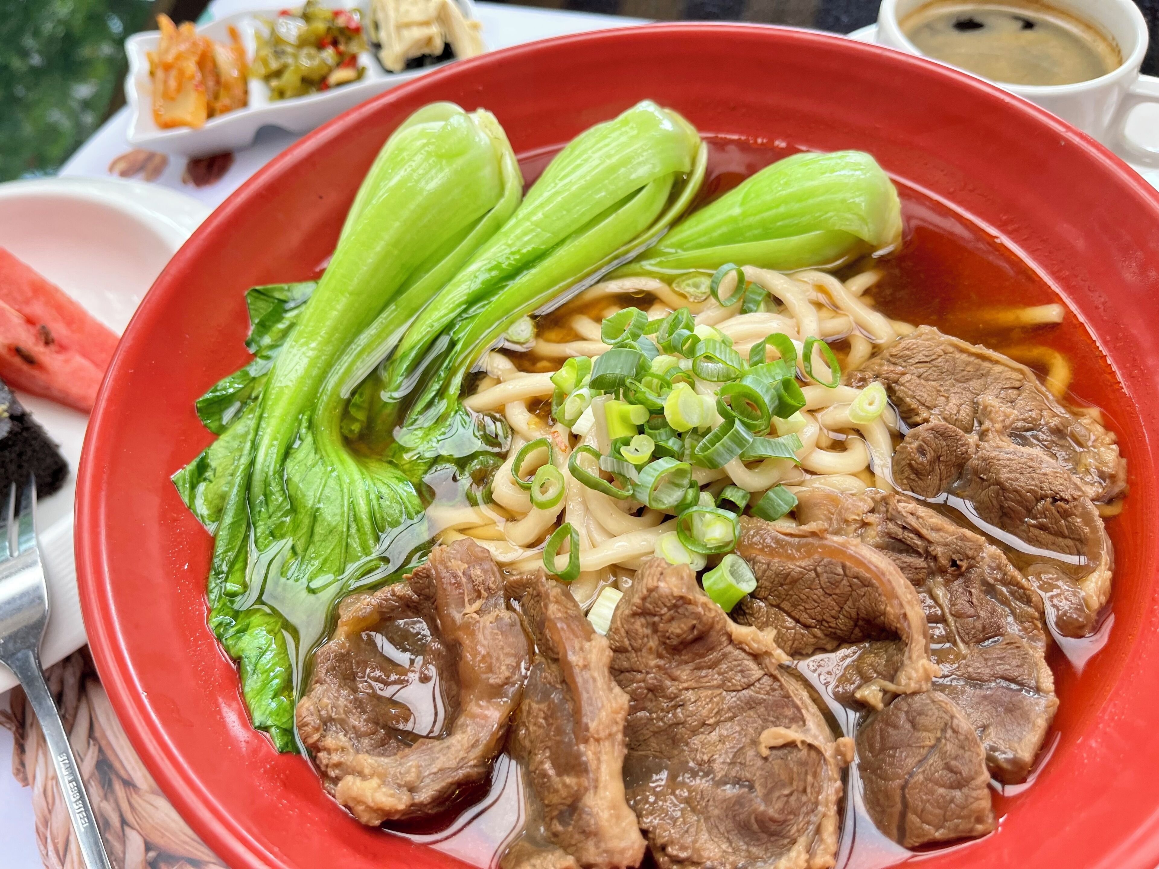Un tazón de ramen con lonjas de carne, cebolletas y bok choy en un tazón rojo.