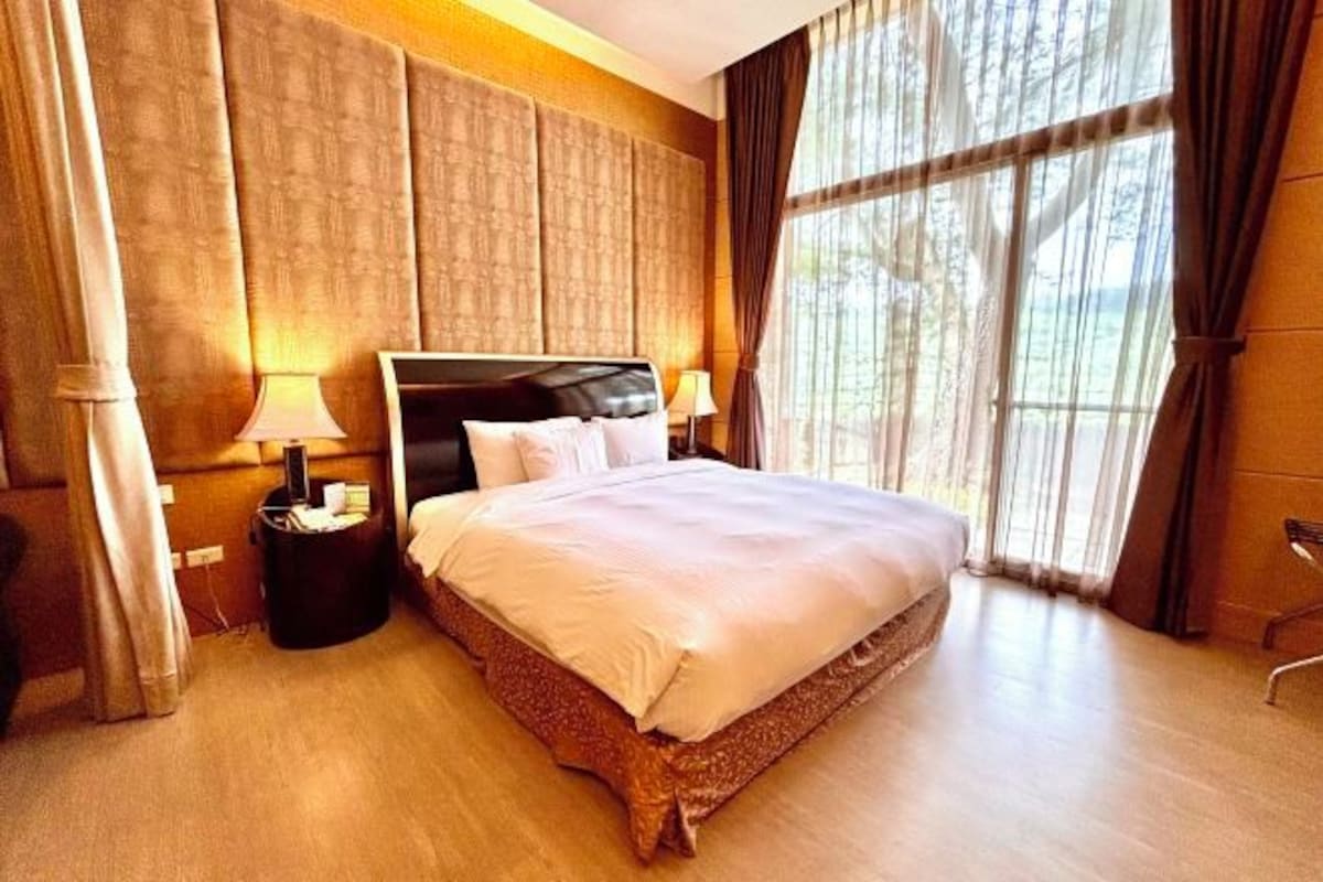 A hotel room with a large bed, two bedside tables, and a window with curtains.