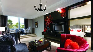 Ein modernes Wohnzimmer mit Sofa, Sessel und Couchtisch. Ein Fernseher und eine rote Blumenkomposition sind an der Wand zu sehen.