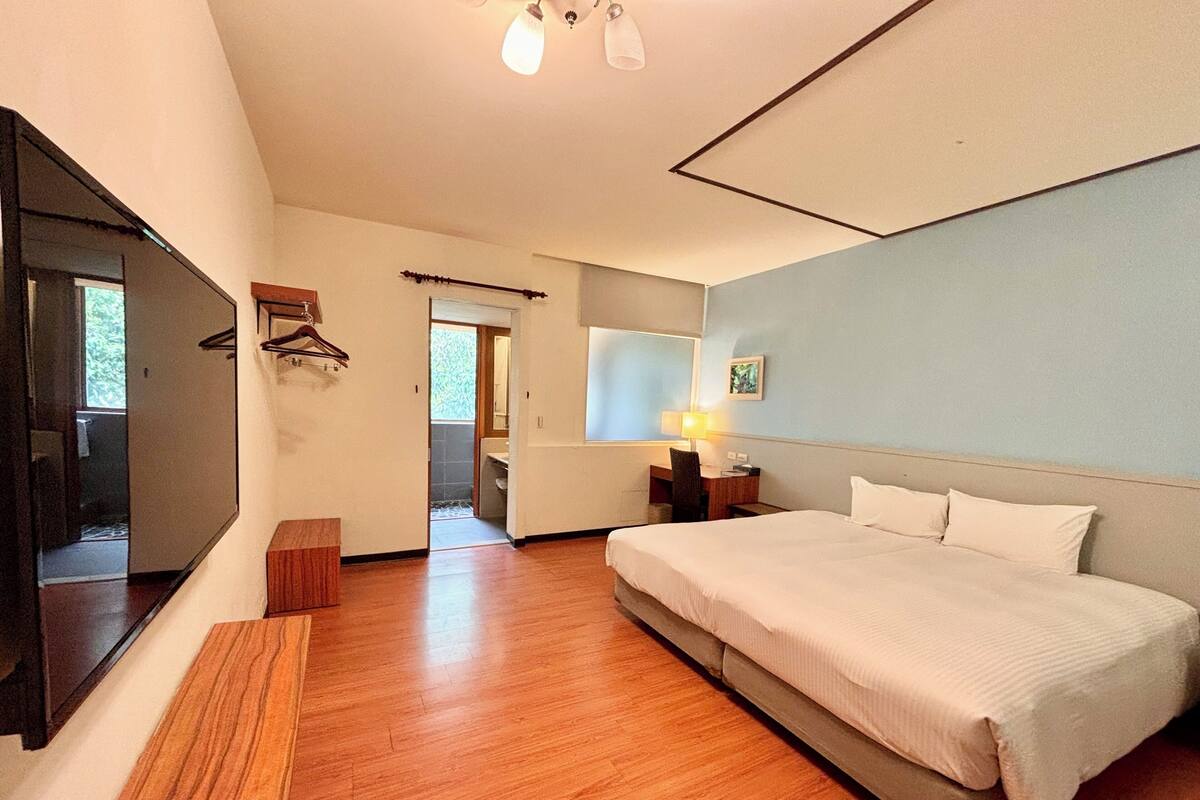 Quarto com cama grande, escrivaninha, cadeira e televisão na parede.