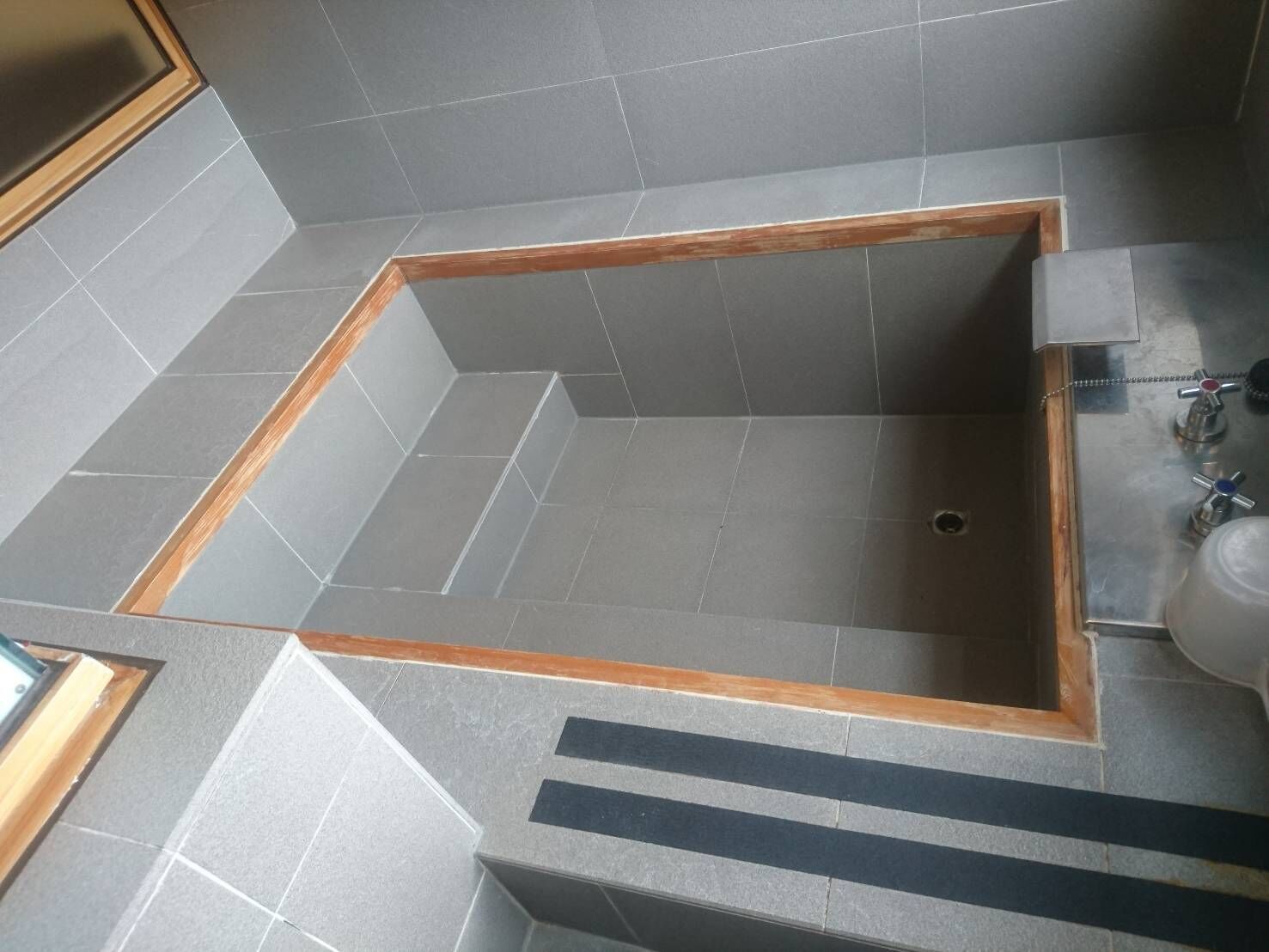 Un baño moderno con una bañera independiente, azulejos grises y un marco de madera.