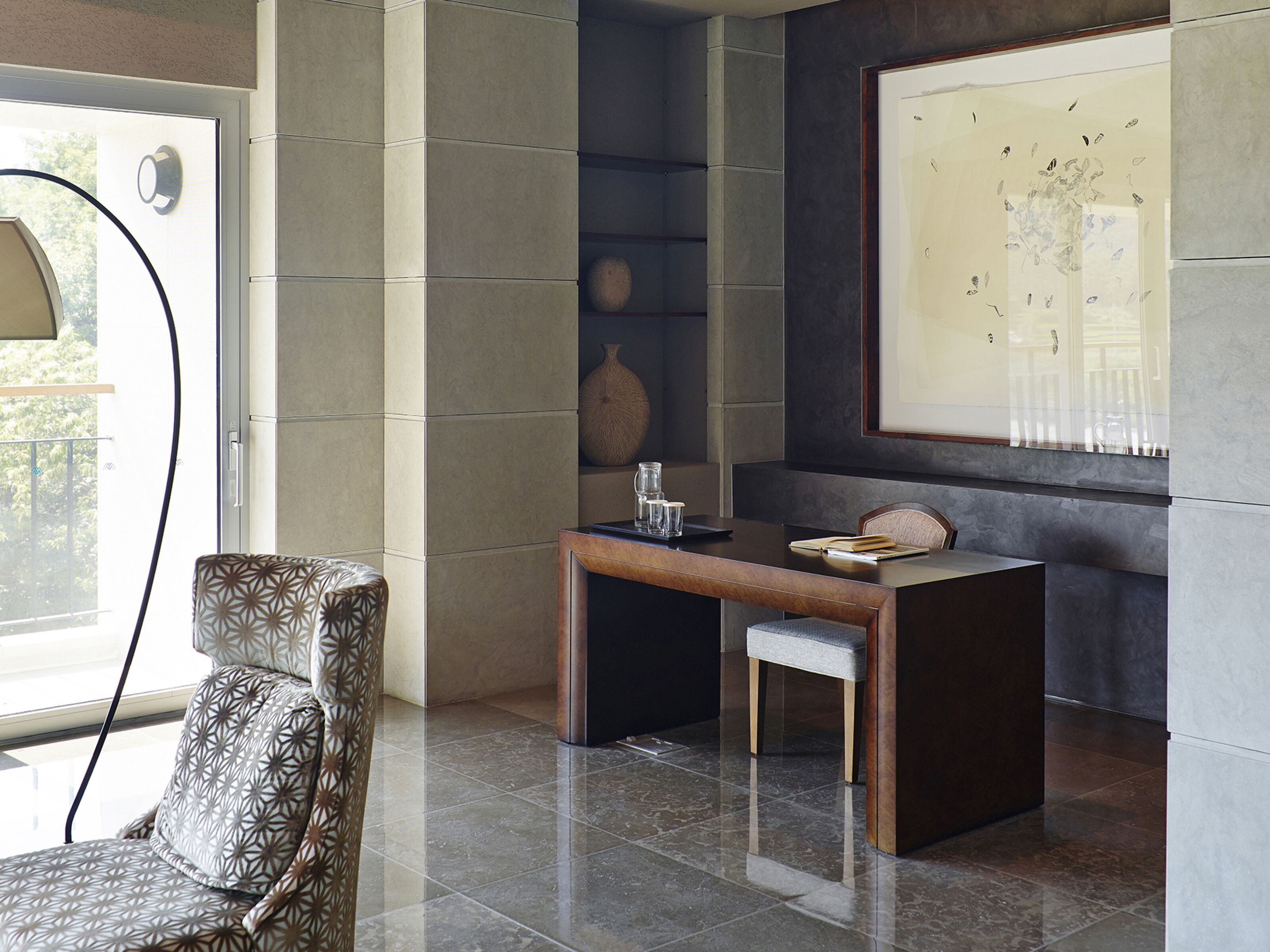 Un interior moderno con un sillón estampado, un escritorio de madera con una silla, y una obra de arte grande enmarcada en la pared.