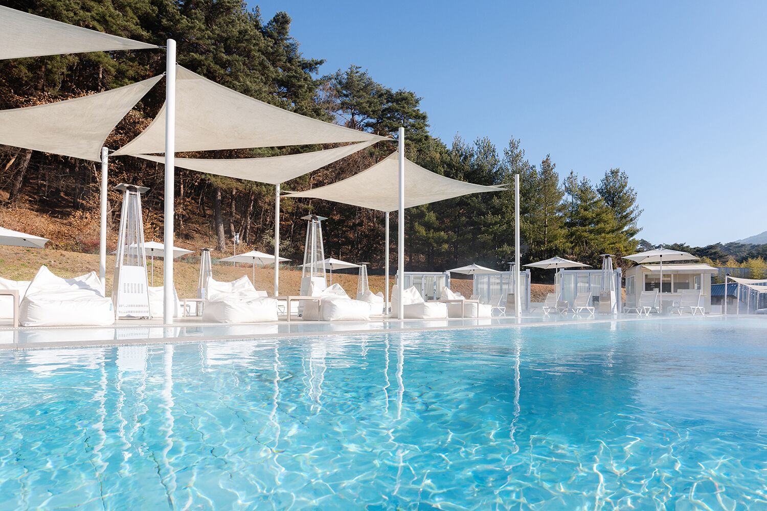 Een zwembad met helder water, parasols en ligbedden.