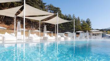 A clear swimming pool with sun umbrellas and lounge chairs.