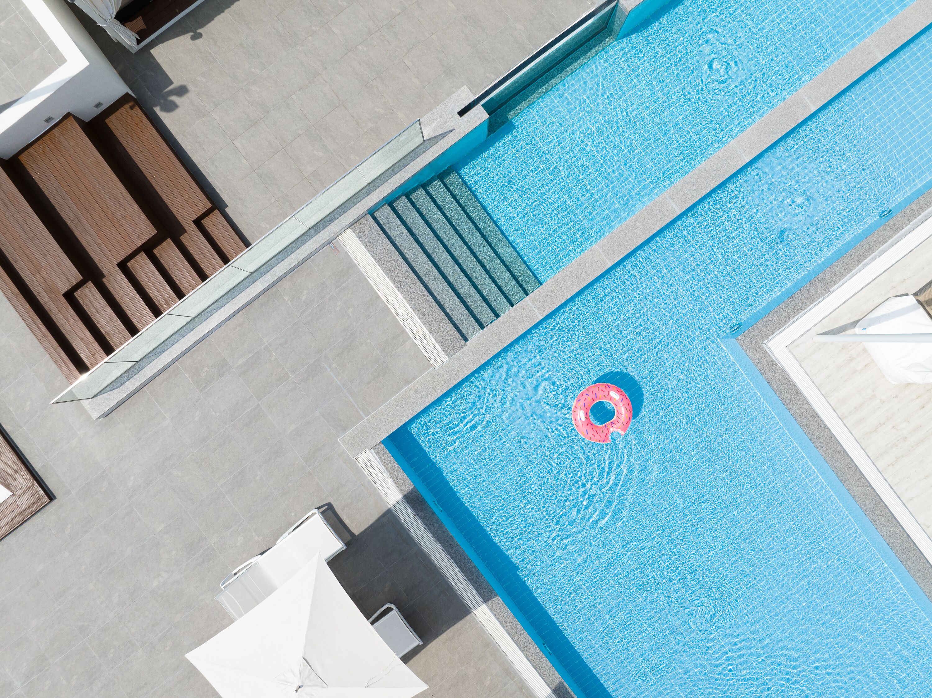 A rooftop pool with a clear blue water surface, a floating pink ring, and a set of stairs leading down to the pool.