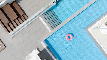A rooftop pool with a clear blue water surface, a floating pink ring, and a set of stairs leading down to the pool.