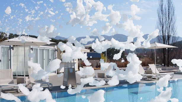 A swimming pool with lounge chairs and umbrellas, surrounded by buildings and mountains. - The Suites Hotel Namwon (Namwon)