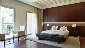 A modern bedroom with a large bed, bedside tables, a desk, and a view of greenery outside.