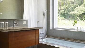 A modern bathroom with a large window, a bathtub, a shower, and a wooden vanity.