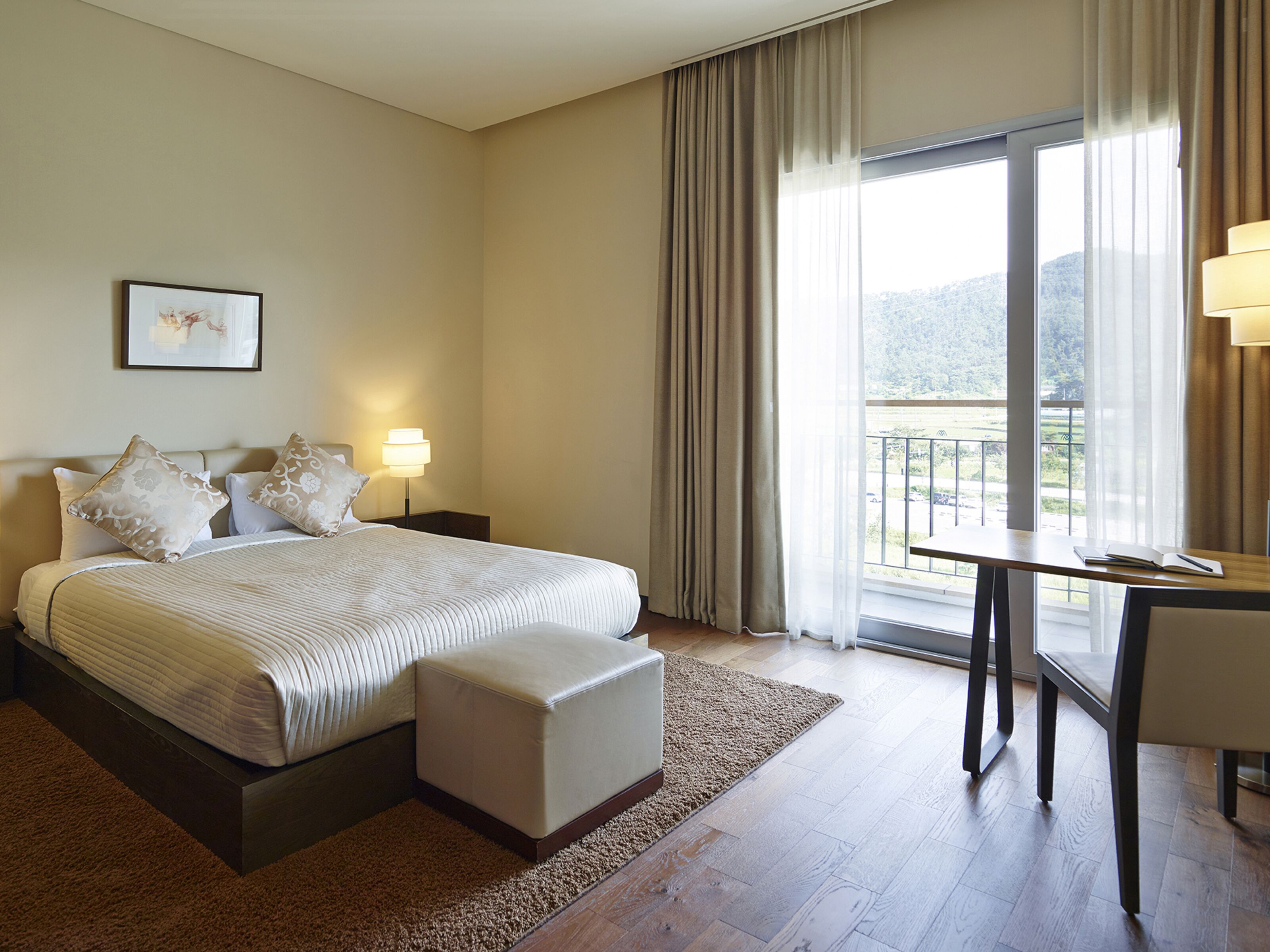 A hotel room with a large bed, a desk, and a view of a balcony.