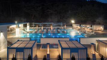 A rooftop pool area with lounge chairs and umbrellas, surrounded by glass walls and a view of the forest.