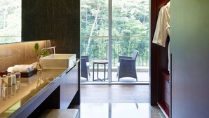 A modern bathroom with a large bathtub, a vanity with toiletries, and a view of a balcony with outdoor furniture. - The Suites Hotel Namwon (Namwon)