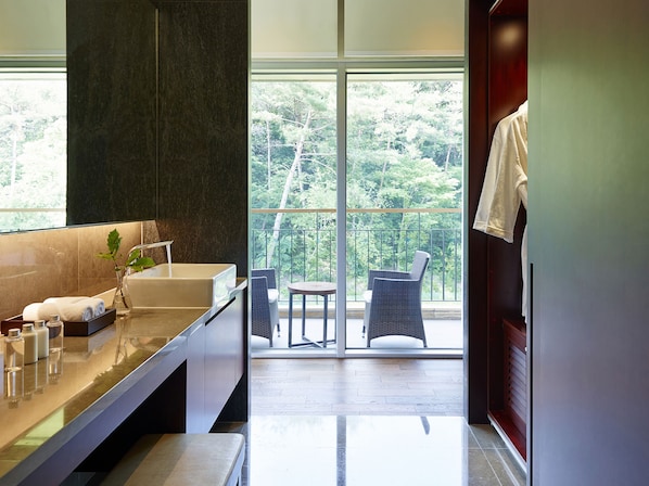Un baño moderno con una bañera grande, un tocador con artículos de aseo y vistas a un balcón con mobiliario exterior.