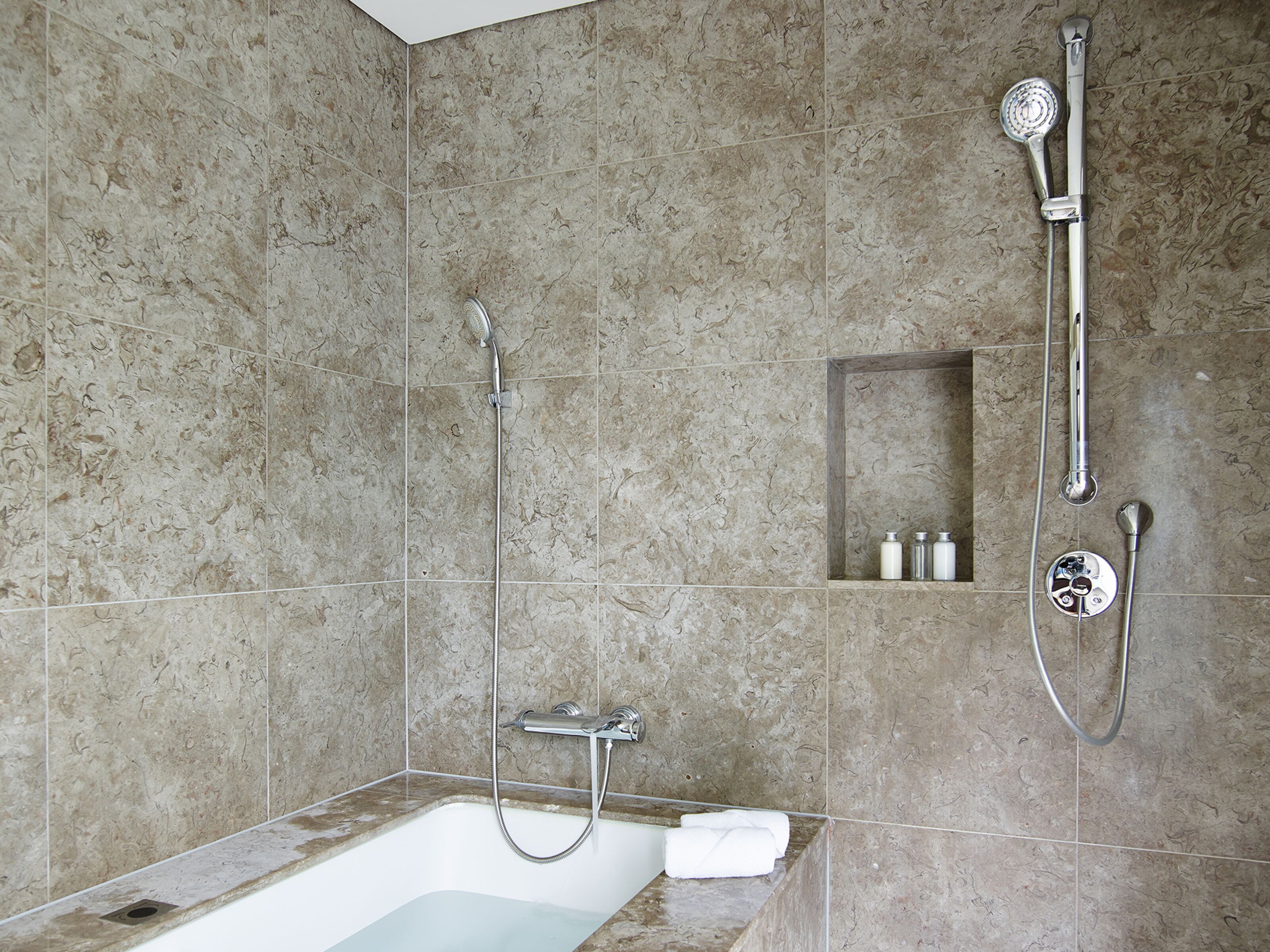 Un baño moderno con bañera, ducha y un estante empotrado con artículos de aseo.