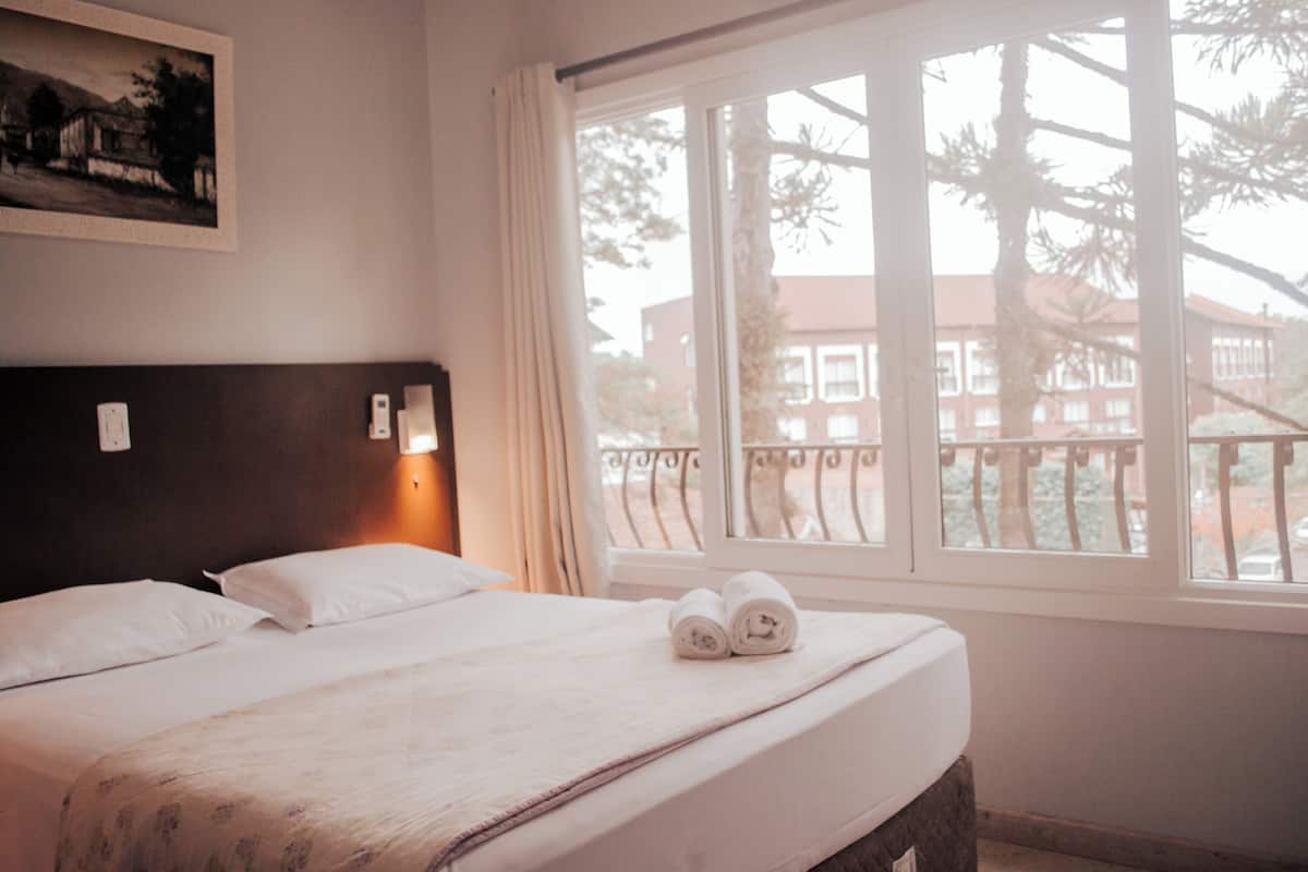 A hotel room with a large bed, a window with a view of buildings, and a painting on the wall.