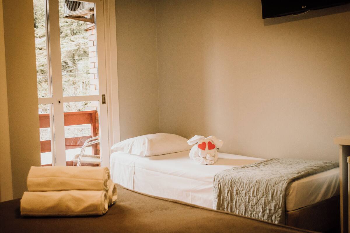 A hotel room with a bed, a window, and a chair.